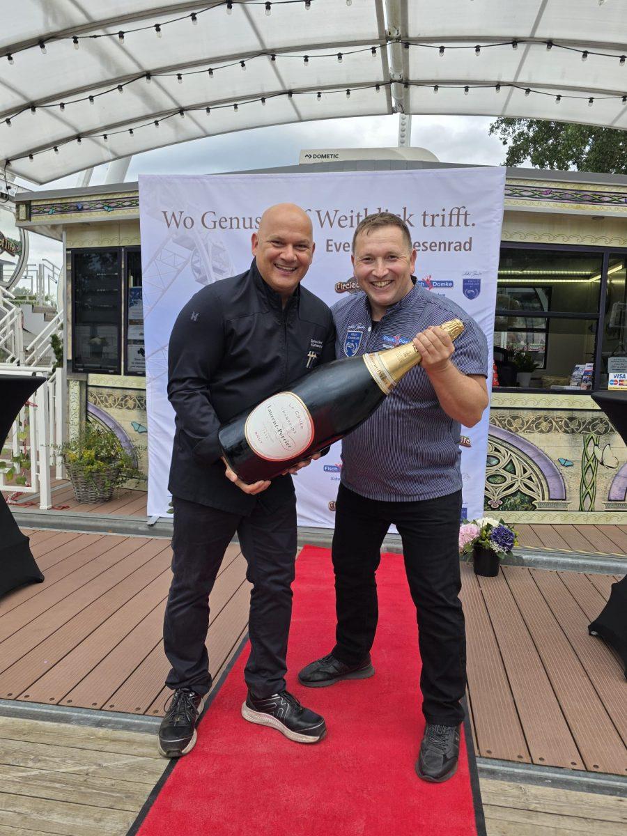 Gast präsentiert eine Champagnerflasche beim Riesenrad Dinner 2026 auf Usedom